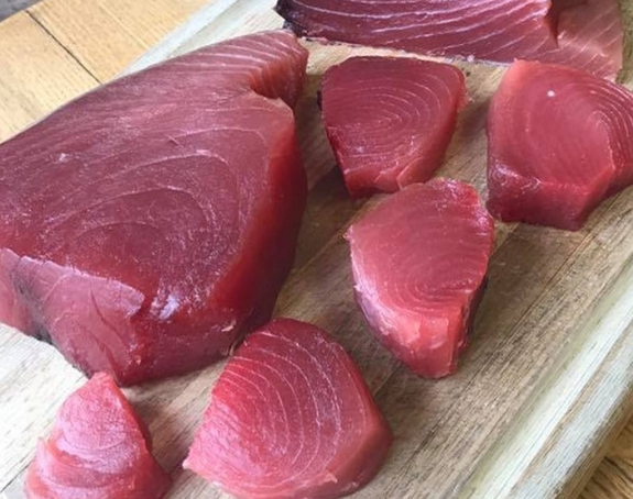 Raw tuna loin cut into medallions on wooden board.