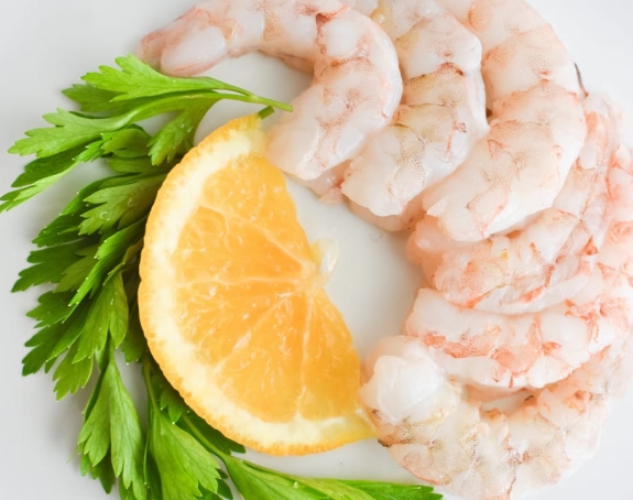 Fresh shrimp with lemon and herbs on white plate – gourmet seafood.